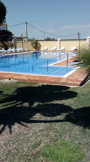 Una piscina con plataforma de baldosas y sillas de descanso.