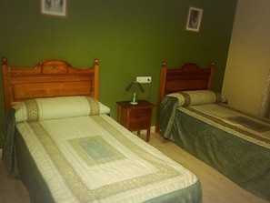A room with two single beds, a nightstand with a lamp, and a green wall. - Hostal Al-Andalus (La Guijarrosa)
