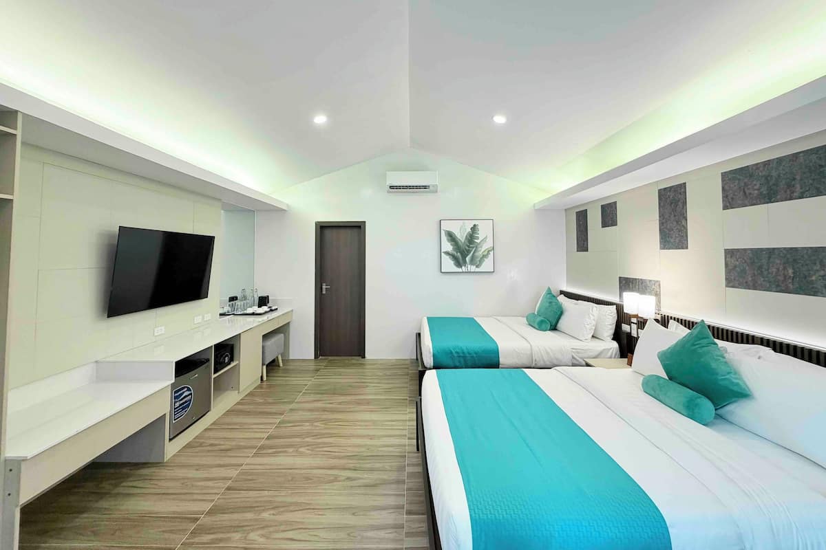 A modern hotel room with a flat-screen TV, a desk with a computer, two beds with teal bedding, and a large window.