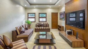 A modern living room with a sofa set, a coffee table, a TV, and a wooden accent wall. - Solina Beach & Nature Resort (Carles)