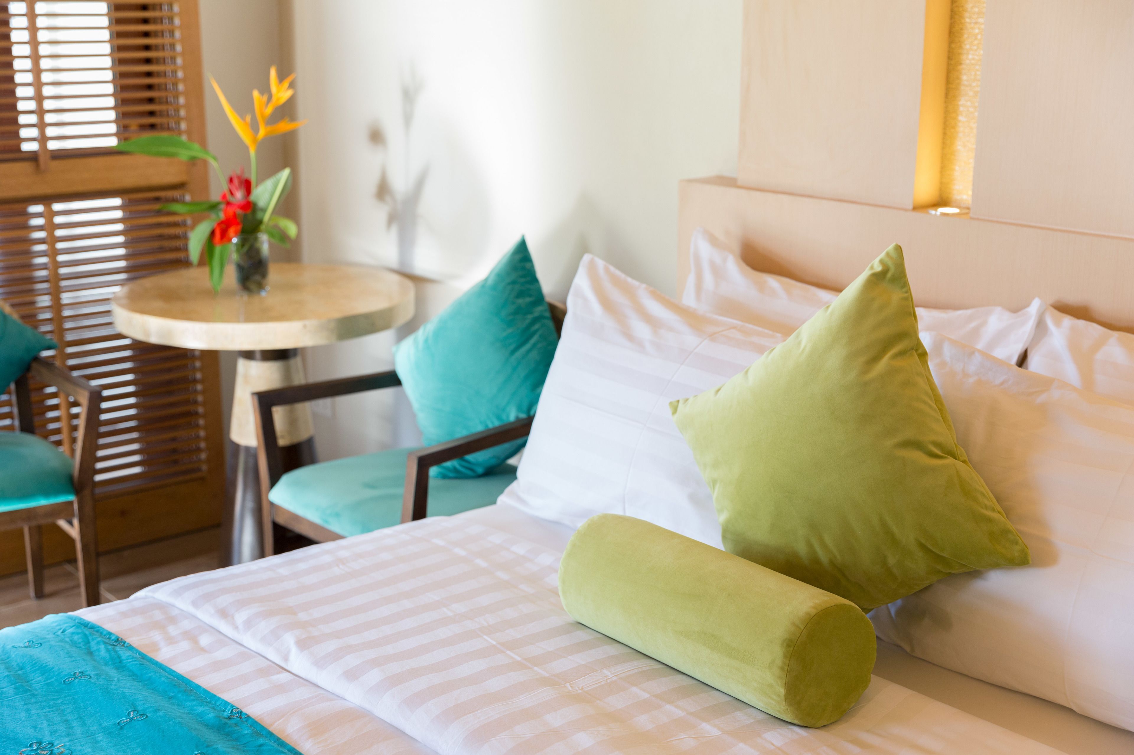 A neatly arranged hotel room with a bed, pillows, a small round table, and a chair.