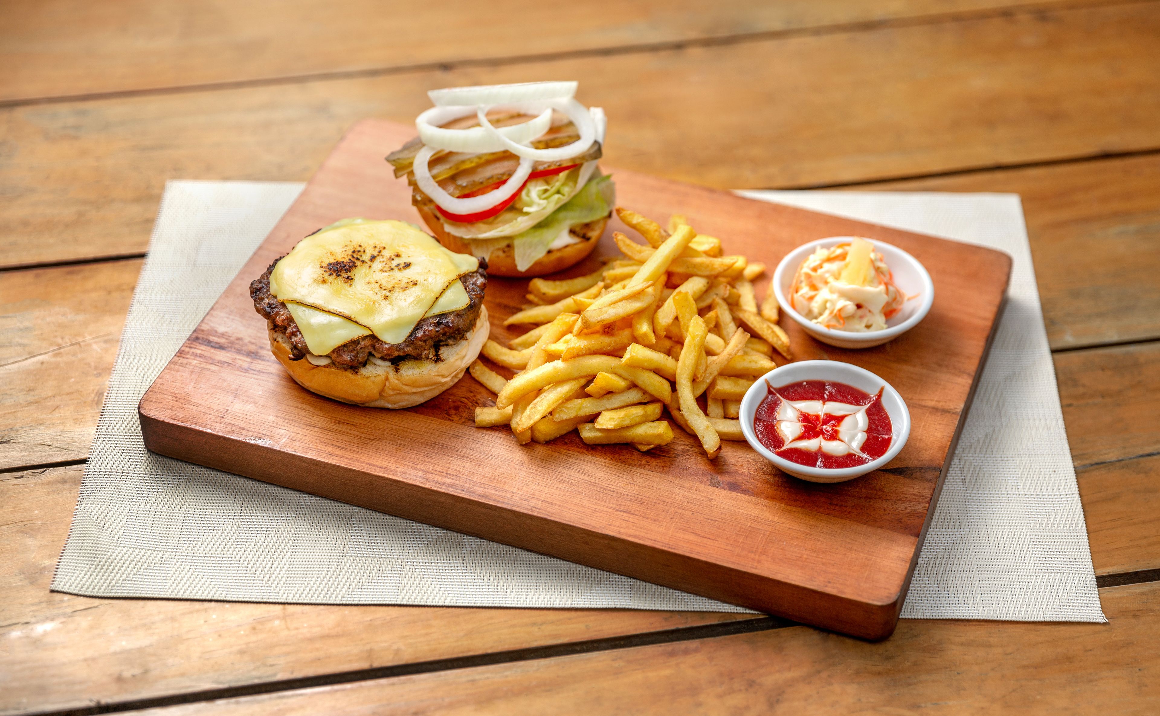 A wooden table with a burger, fries, and two dipping sauces.