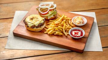 A wooden table with a burger, fries, and two dipping sauces.