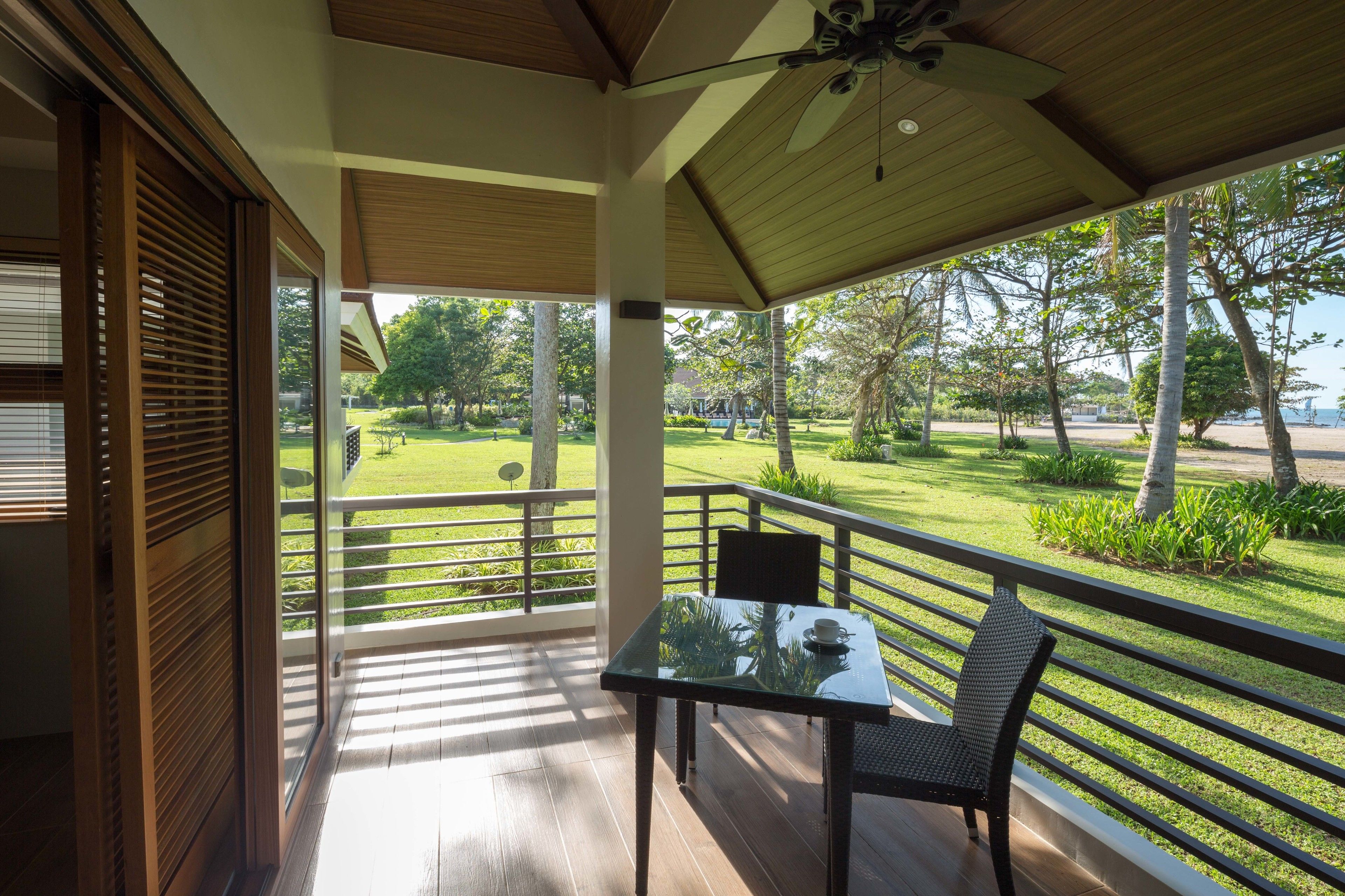 A balcony with a table and chairs, overlooking a well-maintained lawn and trees.
