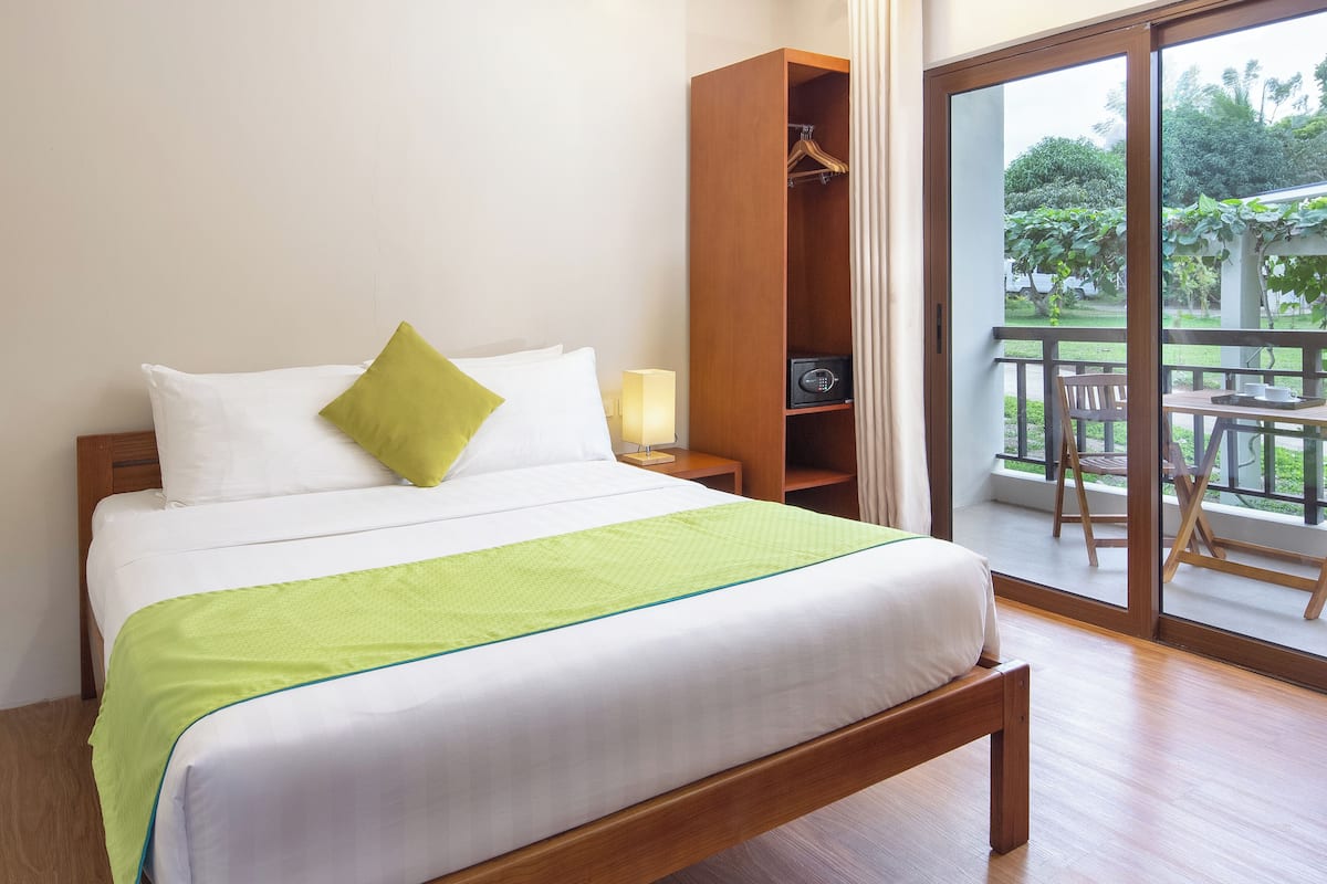 A neatly made bed with a green bedspread, a wooden nightstand with a lamp, and a wardrobe.