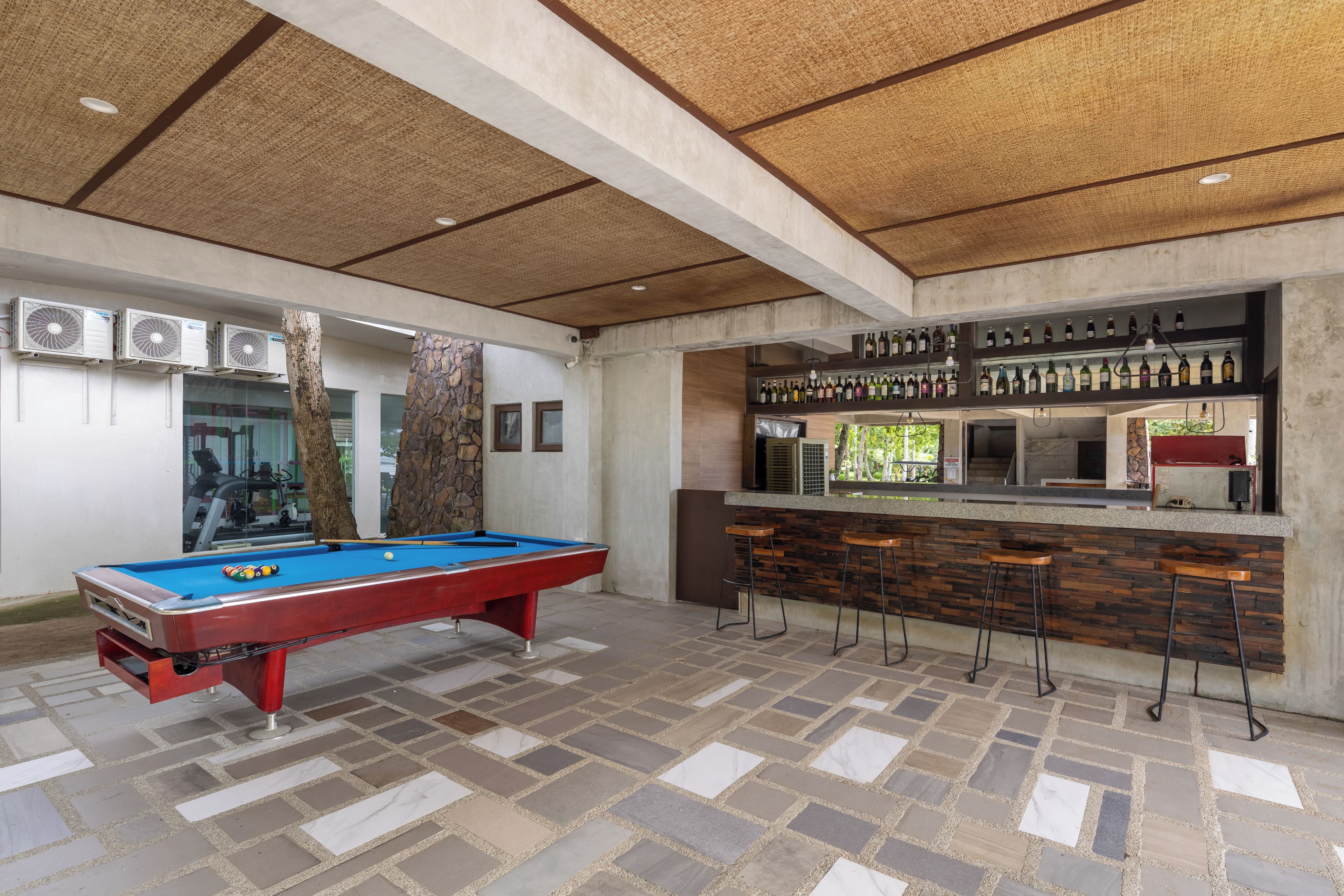 A pool table with a red felt top, a bar area with stools, and a ceiling with a woven pattern.