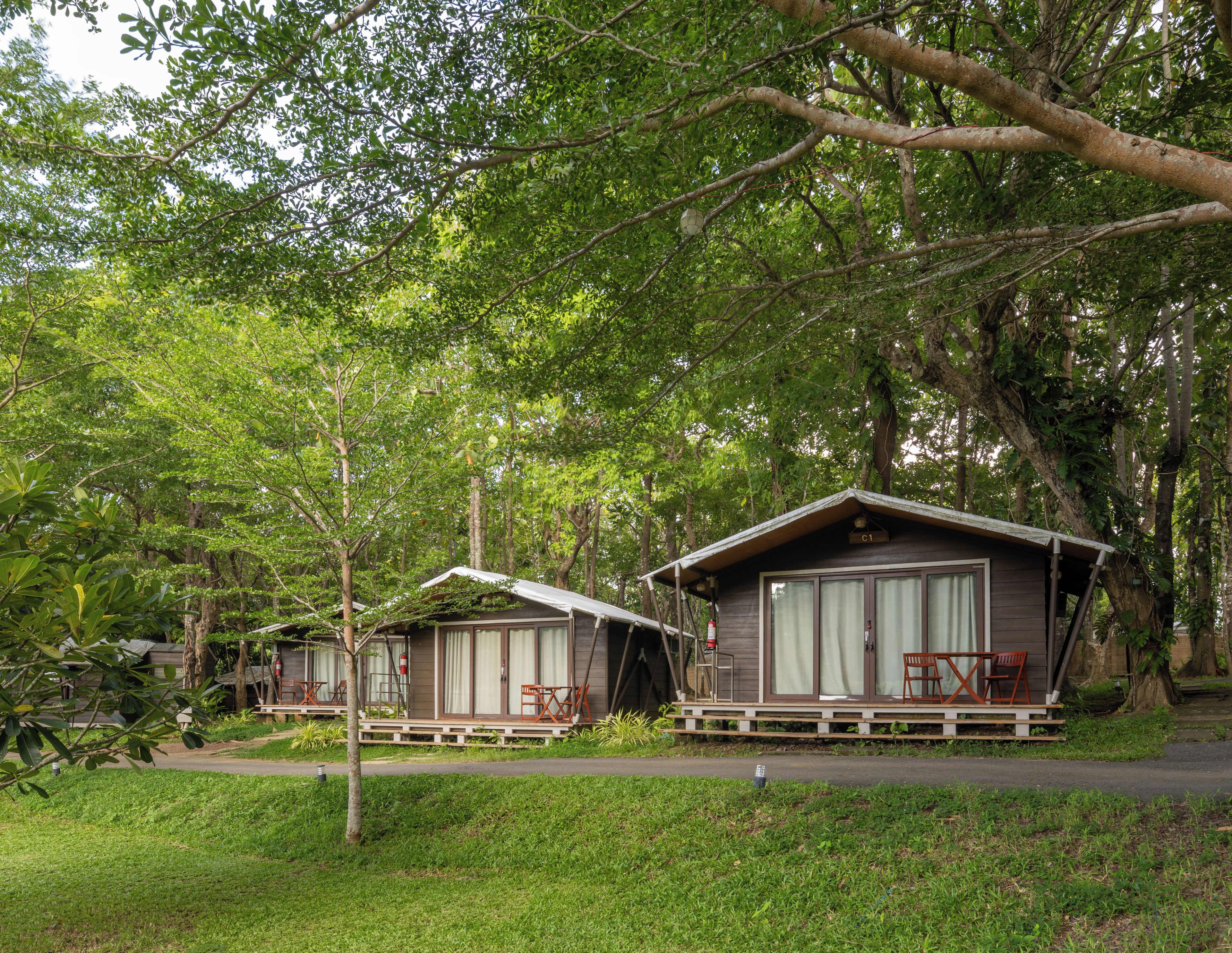 Two cabins with a porch, surrounded by dense greenery.