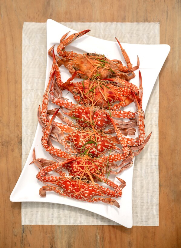 A white plate with several cooked crabs garnished with green herbs, placed on a beige cloth over a wooden surface.