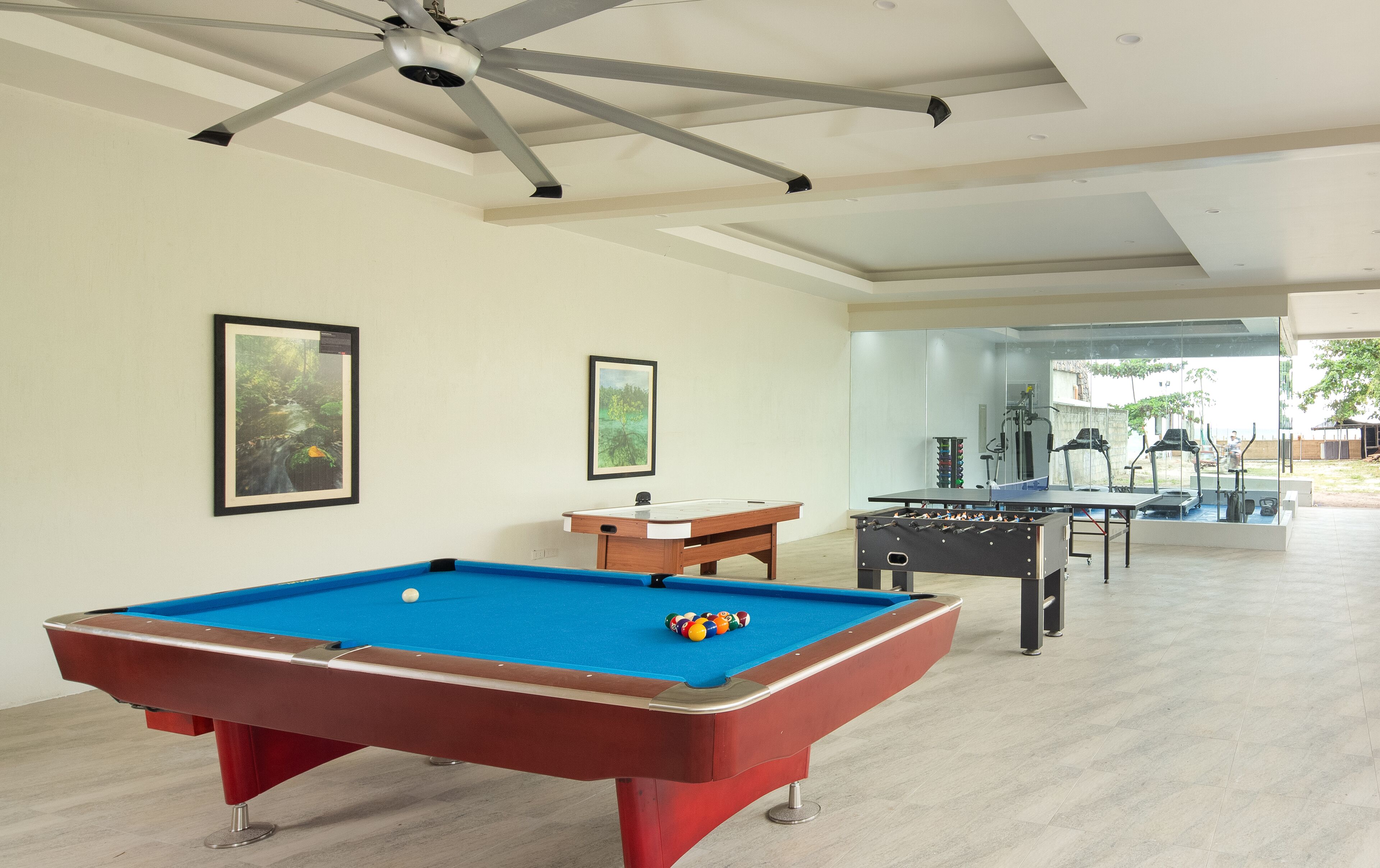 A pool table with a red frame, a ceiling fan, and two framed pictures on the wall.
