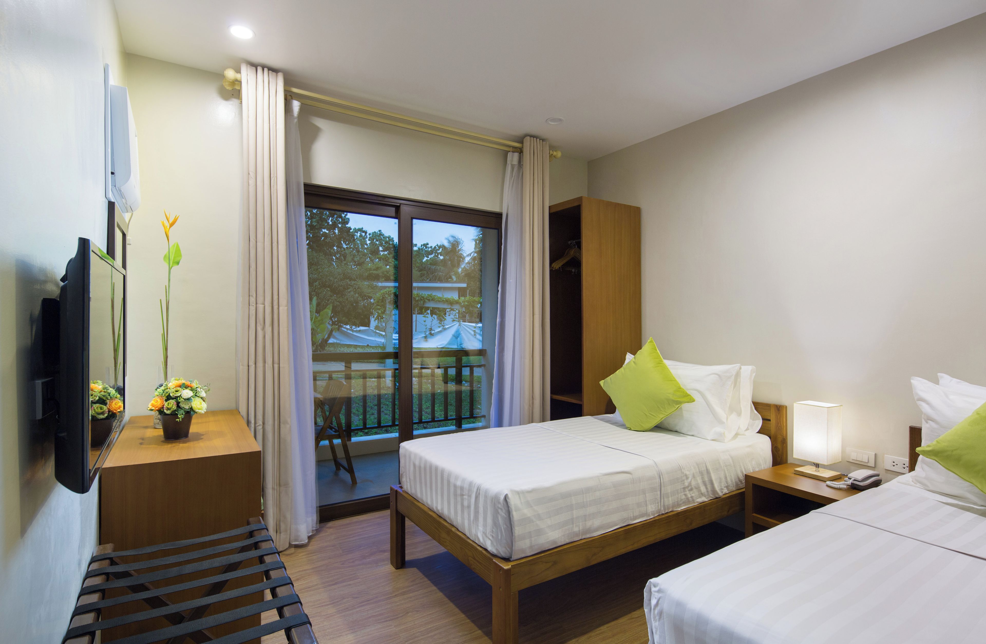 A hotel room with a bed, bedside table, lamp, and a TV mounted on the wall.