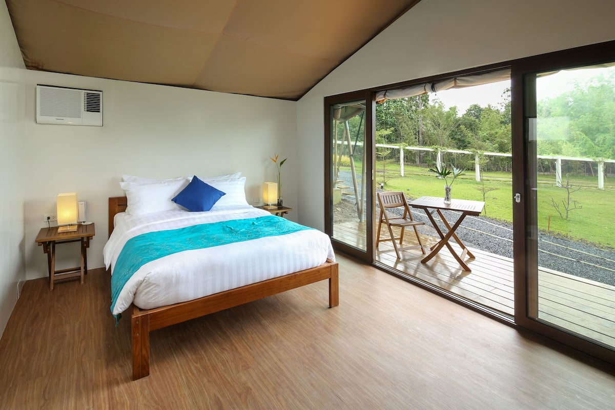 A bedroom with a large bed, a nightstand, a table with chairs, and a sliding glass door leading to an outdoor area.