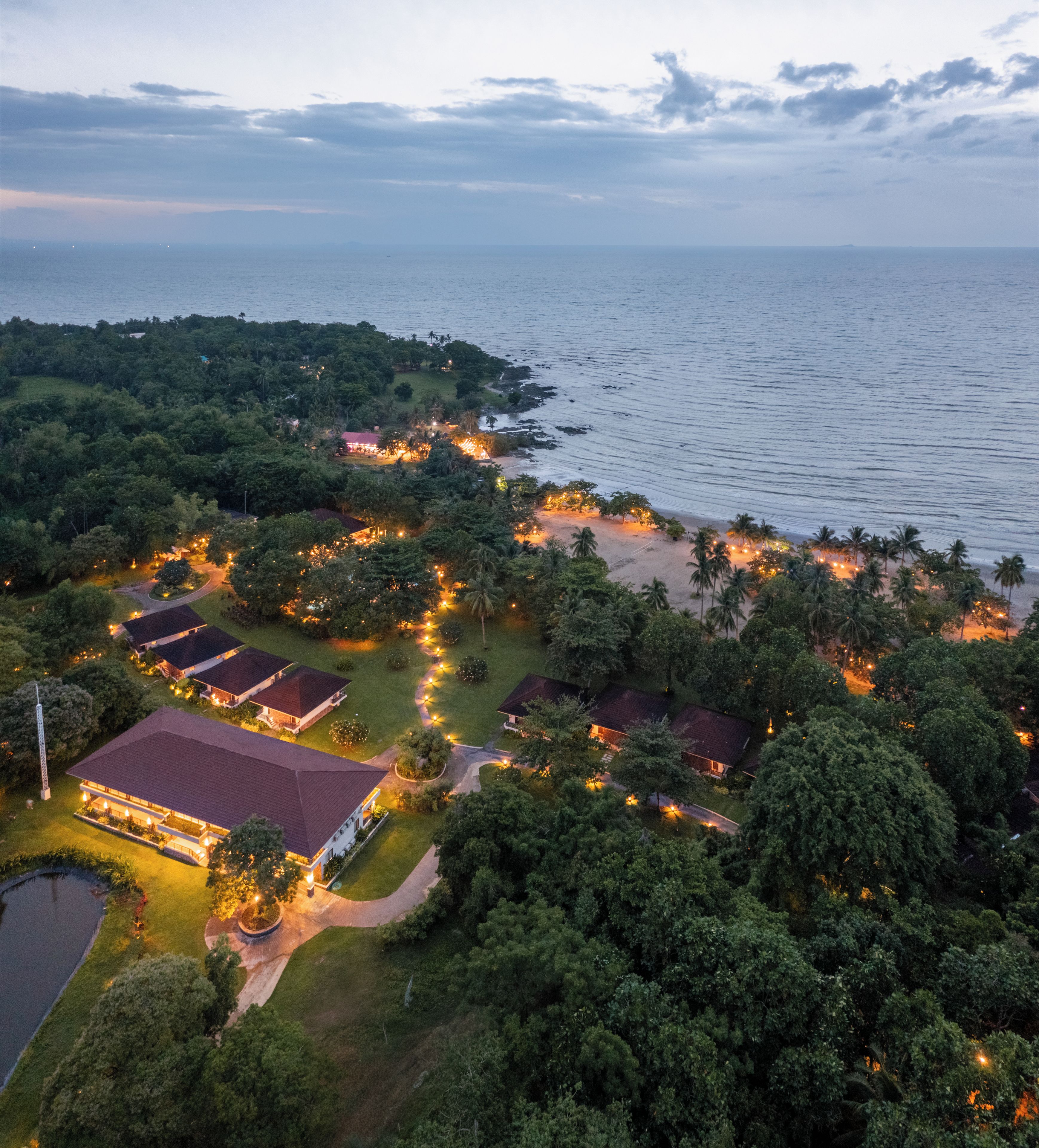 An aerial view of a coastal resort with multiple buildings, pathways, and a beach area.