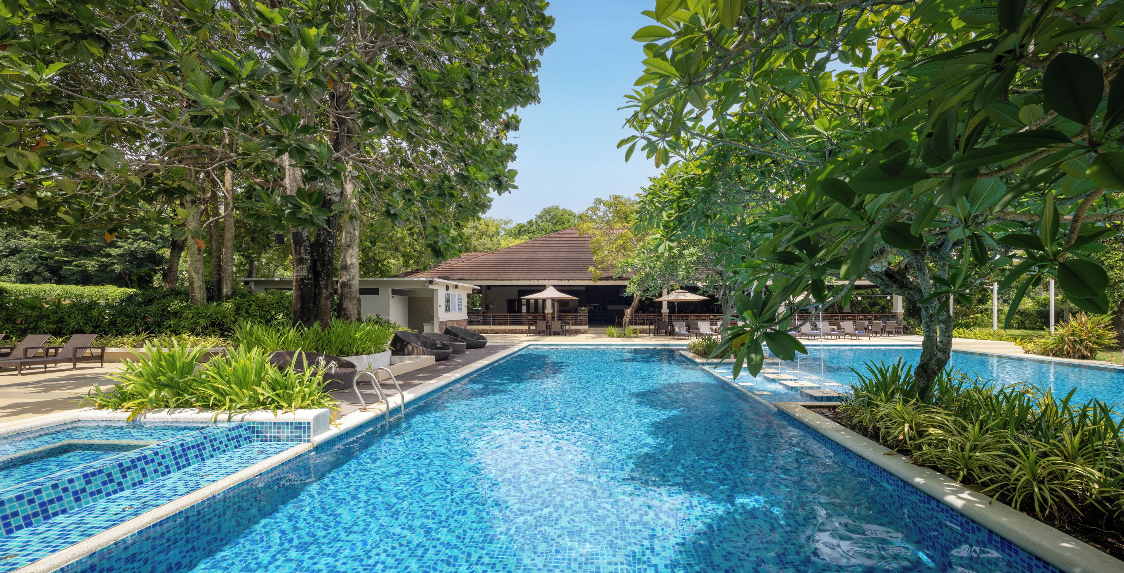 A swimming pool with tiled edges, surrounded by lush greenery and lounge chairs.