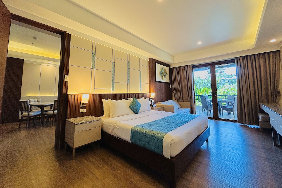 A hotel room with a large bed, a desk, and a balcony with outdoor seating.