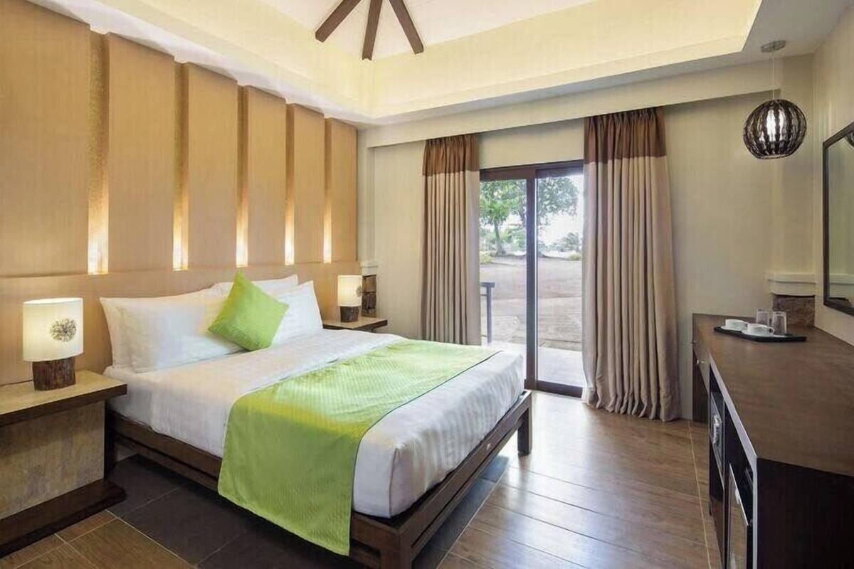 A hotel room with a large bed, a desk, a chair, and a view of the outdoors through a sliding door.