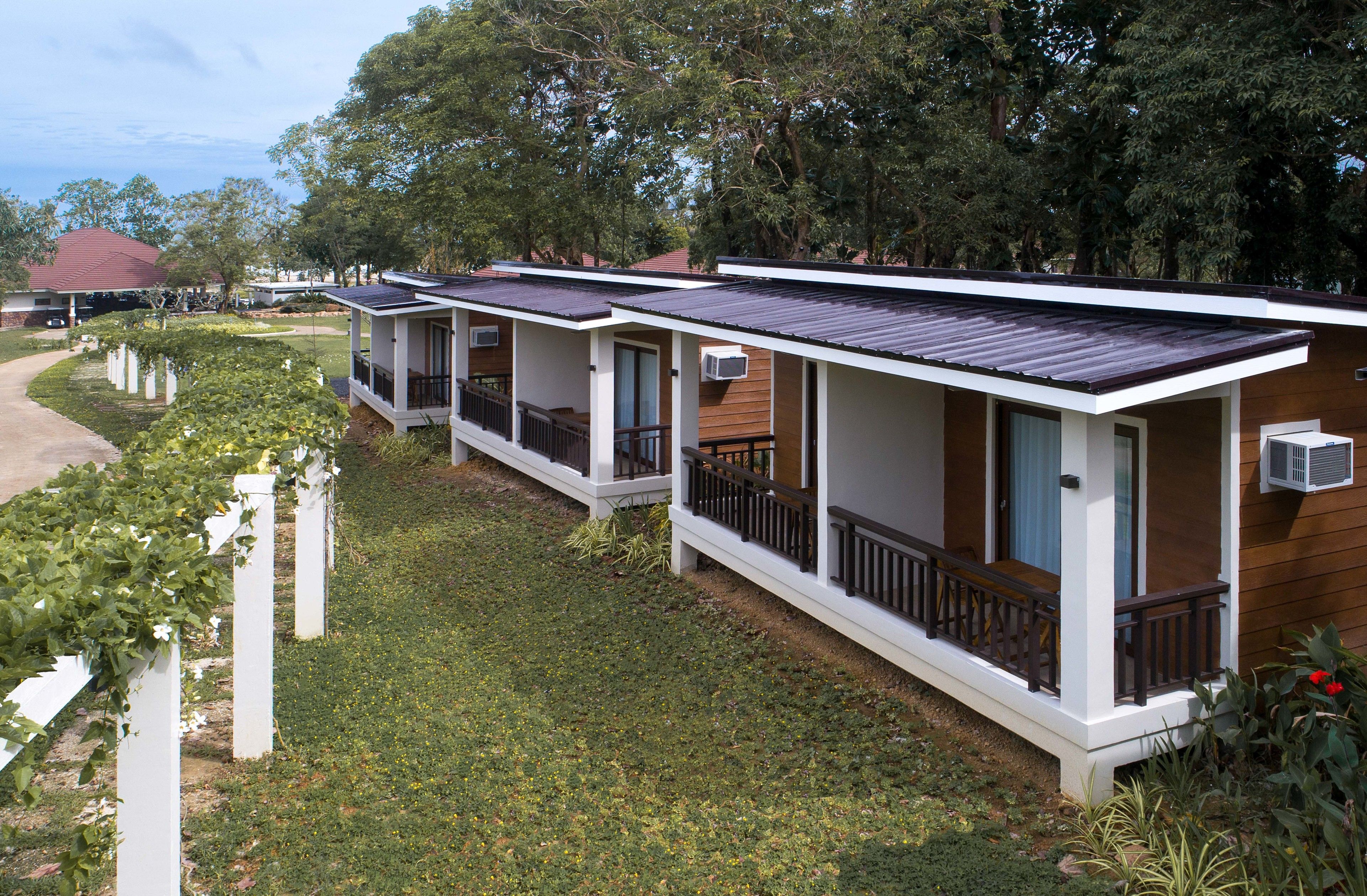 Een rij bungalows met een terrasje, omgeven door groen en bomen.