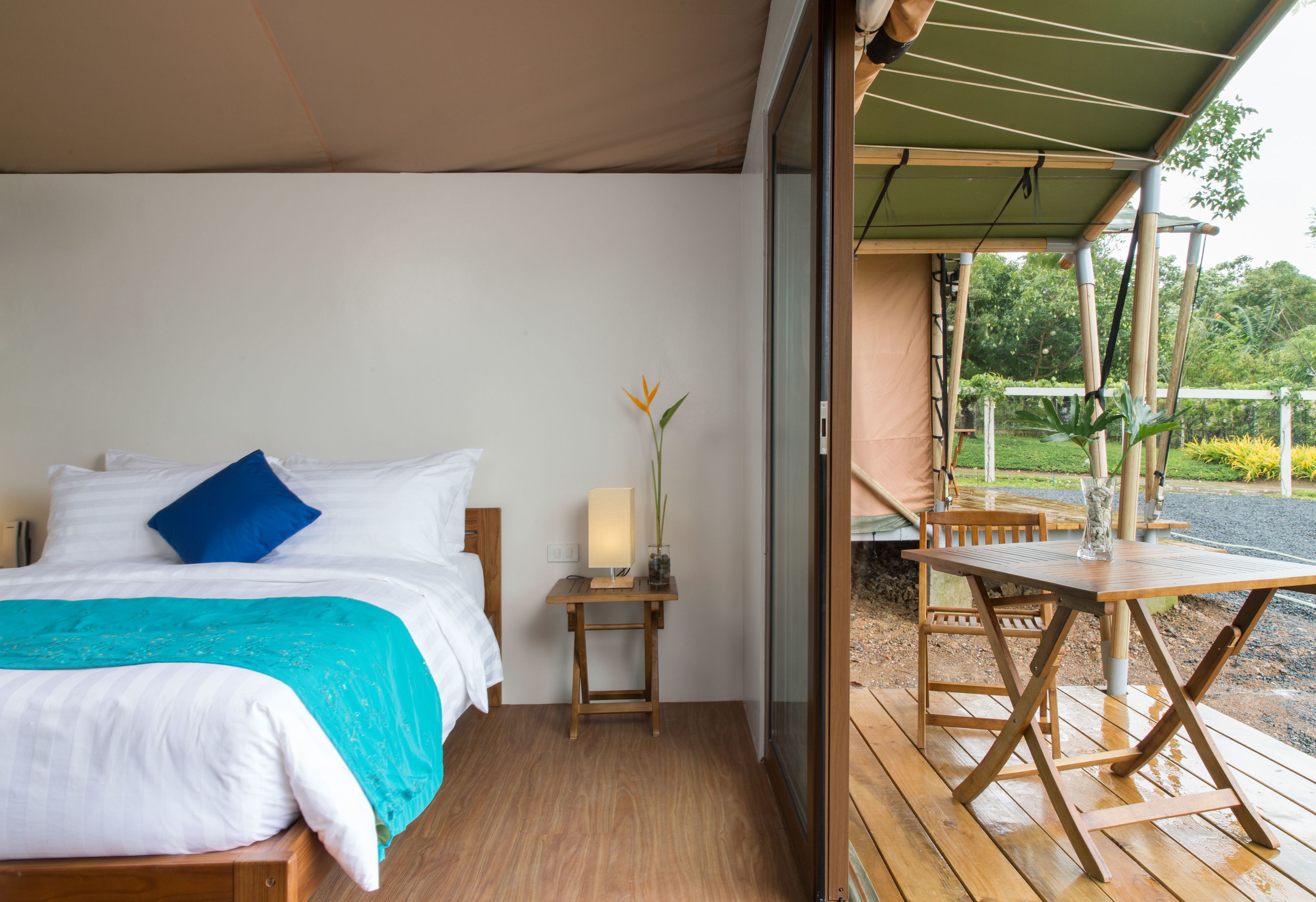 Quarto com uma cama, mesa de cabeceira com abajur e vista para um deque externo.