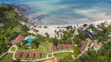 Villas surround a serene courtyard amidst lush greenery and palm trees, offering beach access and ocean views.