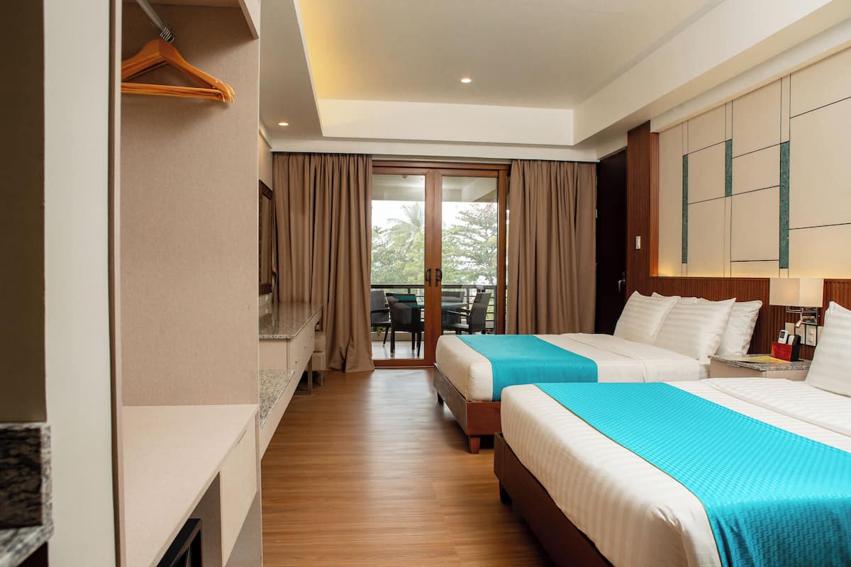 A hotel room with two beds, a desk, and a sliding door to a balcony.