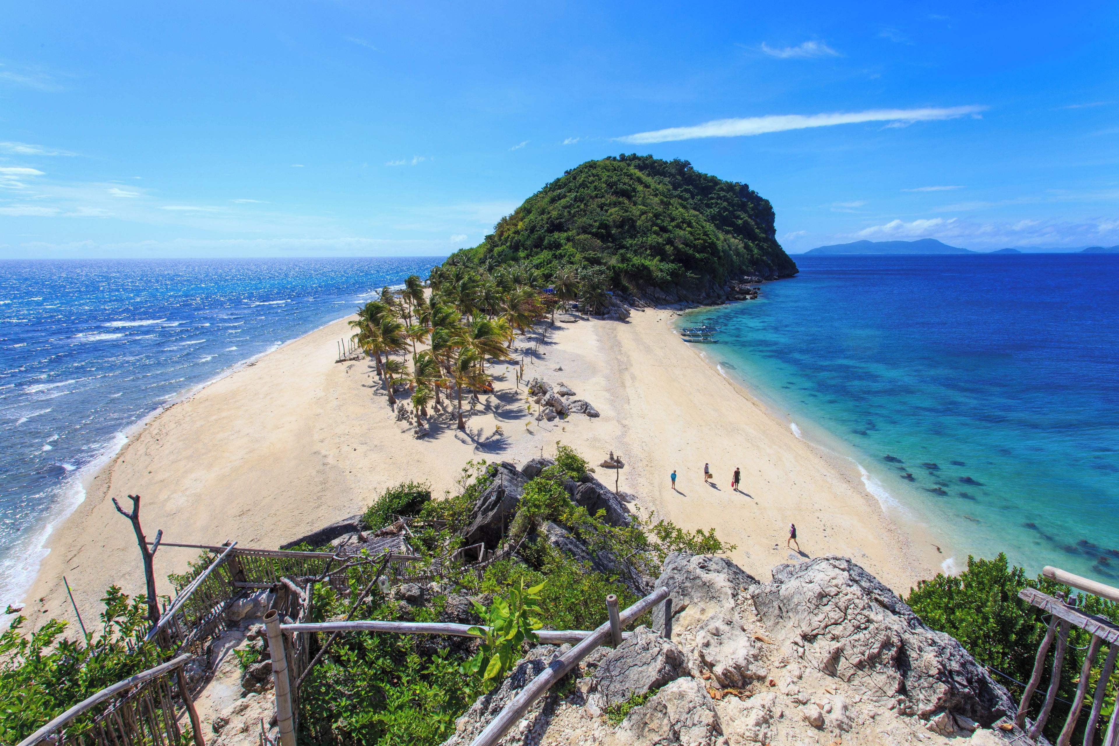 A beach with clear blue waters, a sandy shore, and a small hill with dense vegetation.