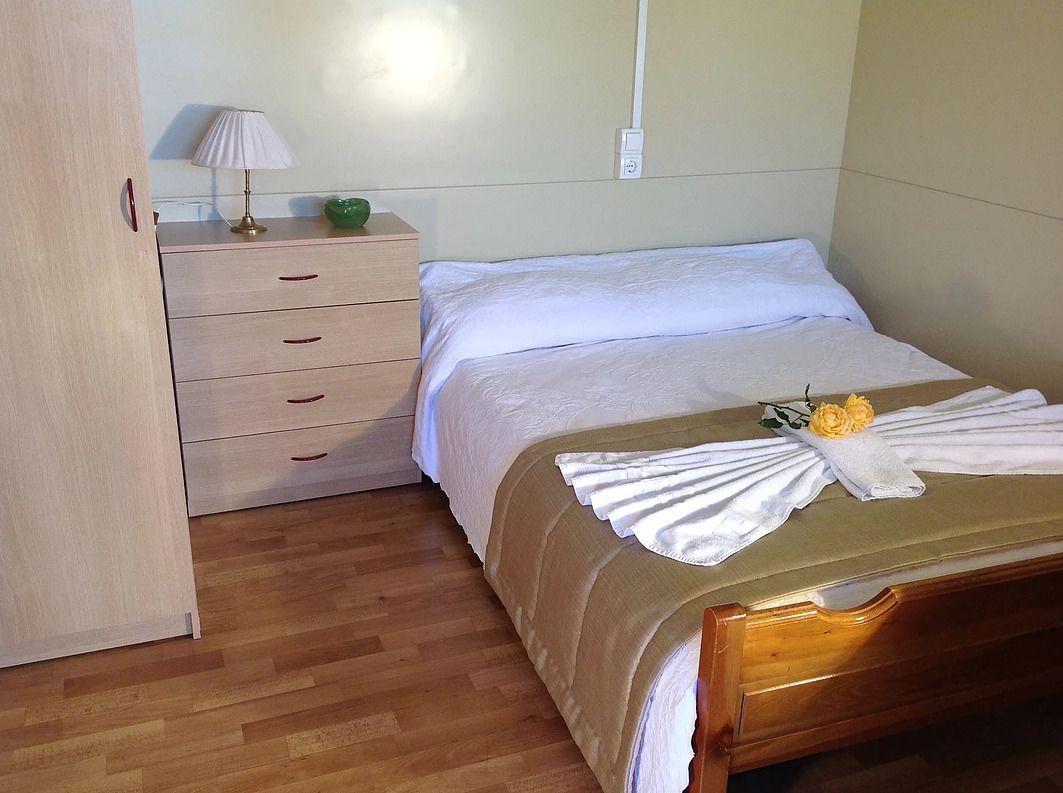 A neatly made bed with a white comforter and a towel with a yellow flower.