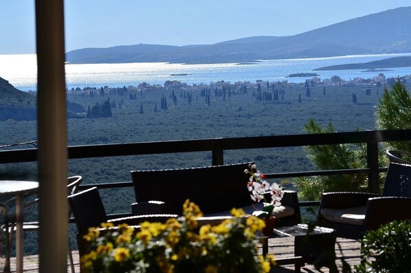 Terraço com área de estar ao ar livre, com vista para a paisagem costeira, colinas e um corpo d'água.