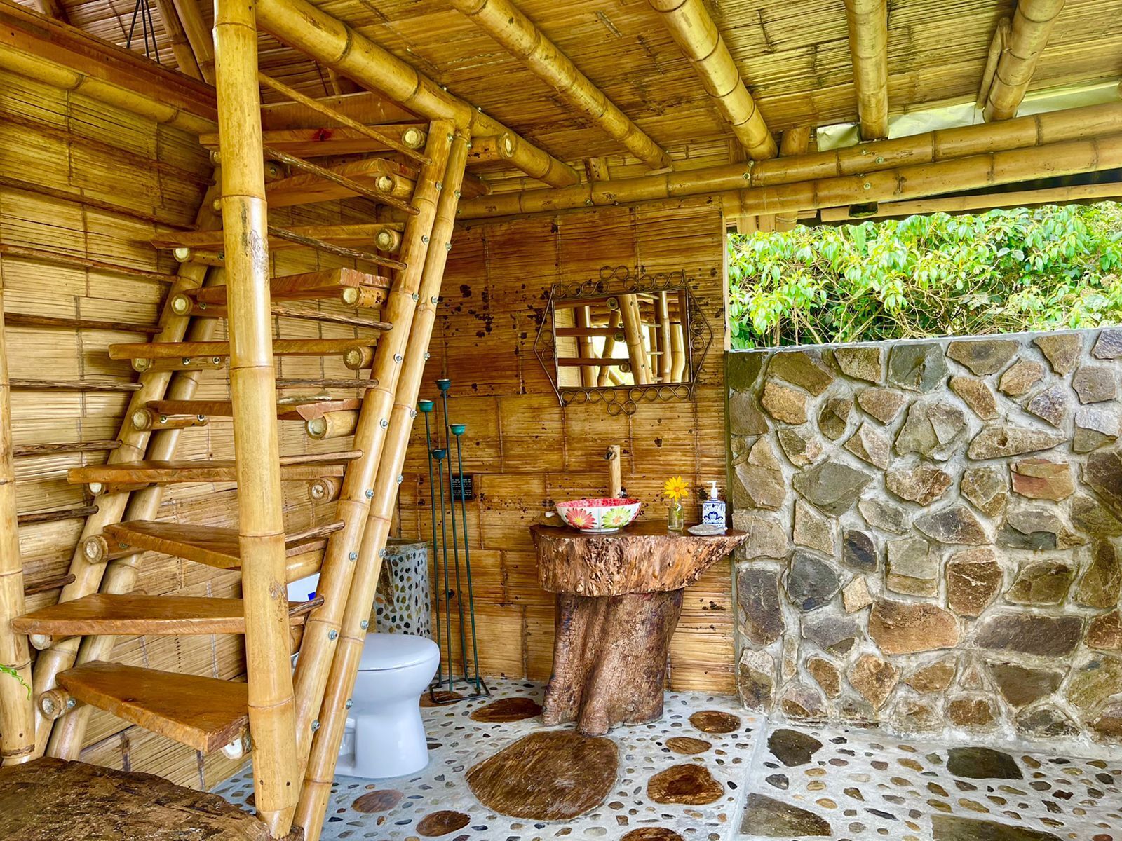 A bamboo interior with a stone wall, a wooden toilet, and a small sink.