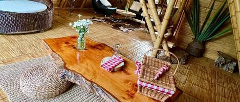 A room with a high ceiling, bamboo structures, a wicker sofa, a wooden table with a vase, and a chair.