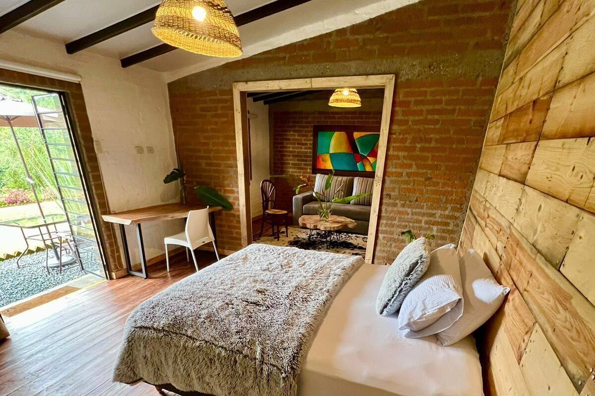 Een moderne slaapkamer met een houten vloer, een groot bed met een witte dekbedovertrek, een houten hoofdbord en een hanglamp.