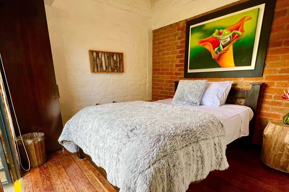 Een slaapkamer met een houten vloer, een bed met een witte deken, een bakstenen muur en een schilderij van een kikker.