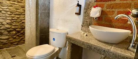 A bathroom with a stone wall, a white toilet, a sink with a mirror, and a towel rack.