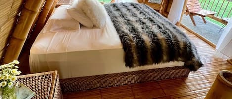 A cozy, wooden-paneled room with a bed, a wicker side table, and a view of the outdoors.
