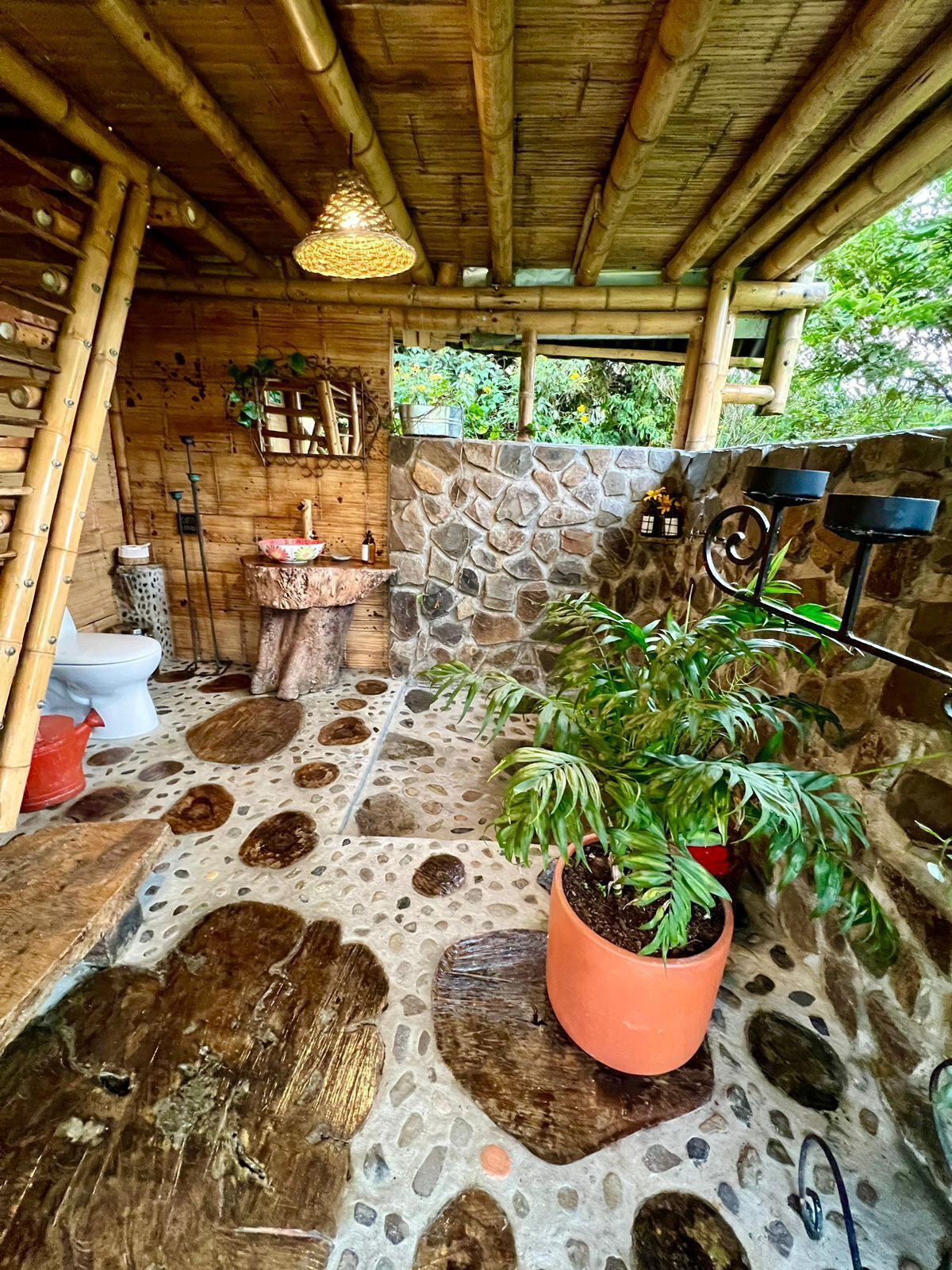 A rustic bathroom with a stone wall, a wooden ceiling, and a potted plant.