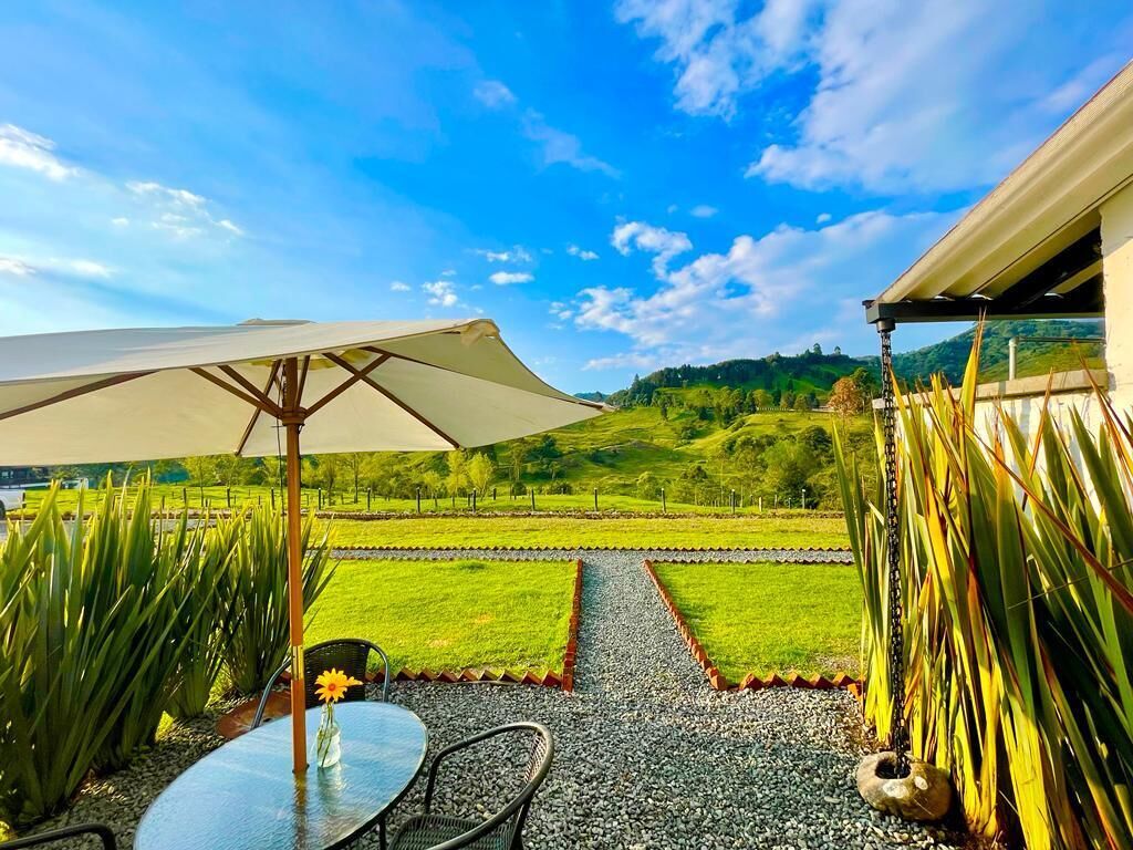 Un patio con tavolo e sedie, un ombrellone grande e vista su un paesaggio verde.