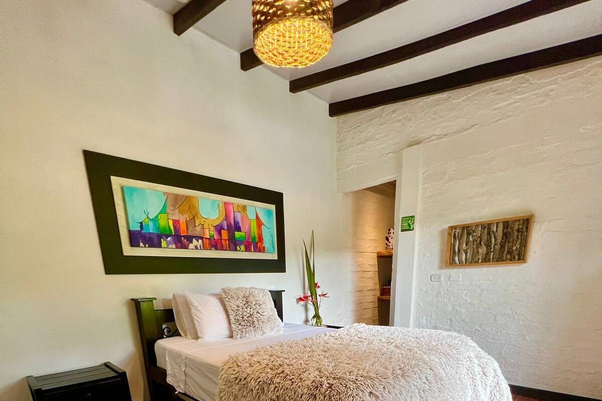 Een slaapkamer met een bed, nachtkastje, stoel, schilderij en een houten vloer.