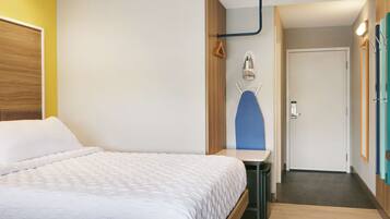 A hotel room with a bed, a small table, a mirror, and a door leading to another room.
