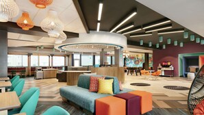 A modern hotel lobby with a central seating area, a reception desk, and a colorful mural. - Tru by Hilton Williamsville Buffalo Airport (Buffalo)