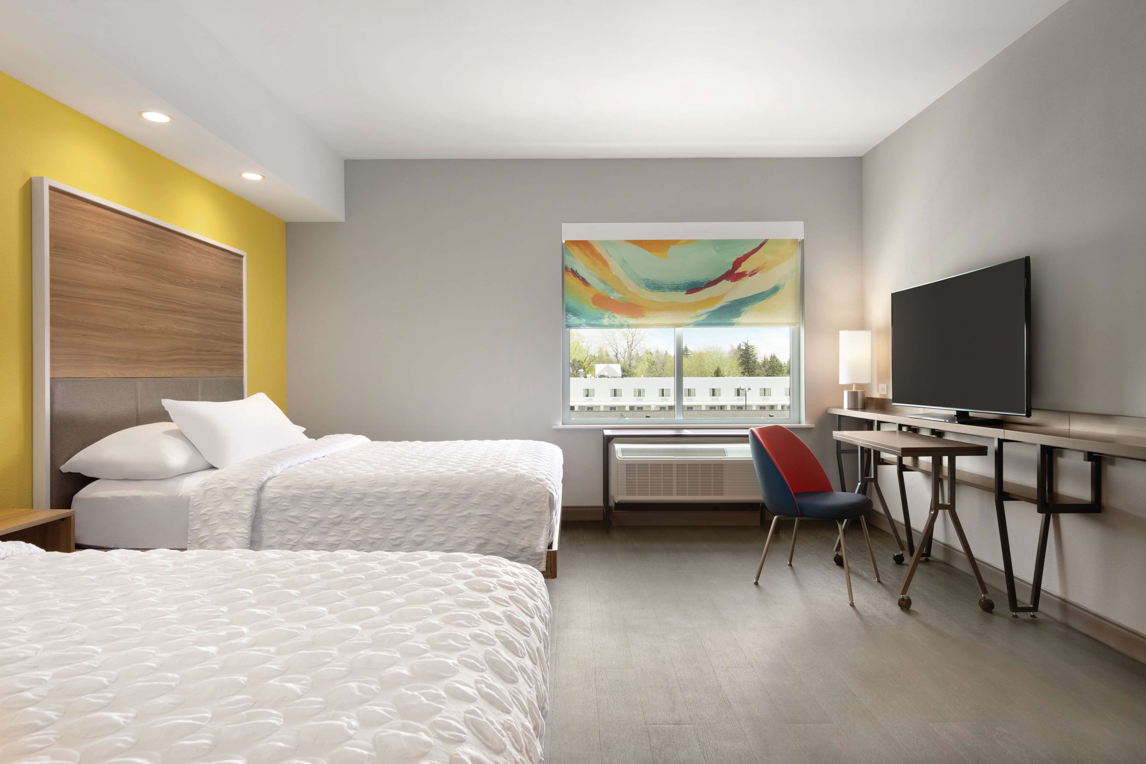 A hotel room with two beds, a desk, a TV, and a large window with a view.