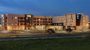 A multi-story hotel with a modern design, featuring a prominent 'HOME 2' sign, a 'tru' logo, and a well-lit entrance. - Tru by Hilton Williamsville Buffalo Airport (Buffalo)