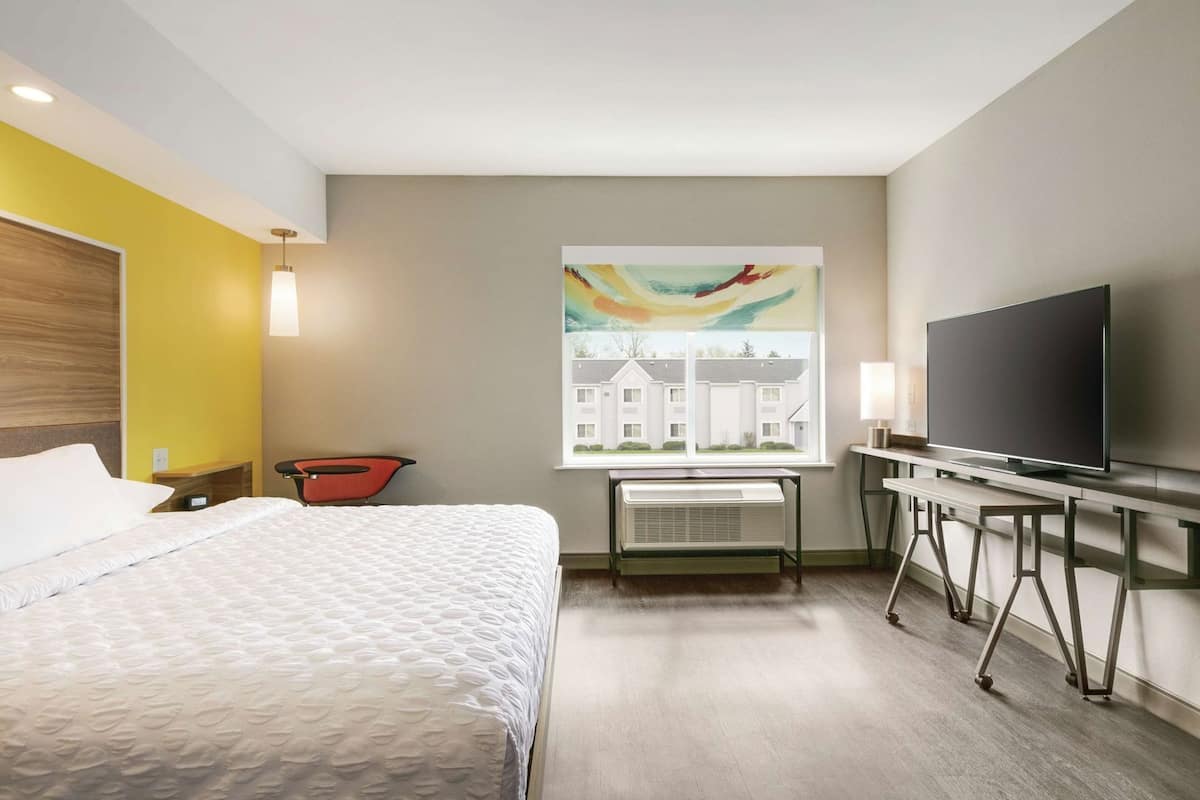 Une chambre d’hôtel avec un lit, une télévision, une fenêtre donnant sur le paysage urbain, un fauteuil rouge et un radiateur.