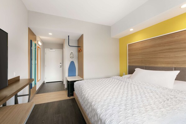 Habitación de hotel con cama, escritorio y espejo. Hay una puerta que conduce a un baño y un perchero.