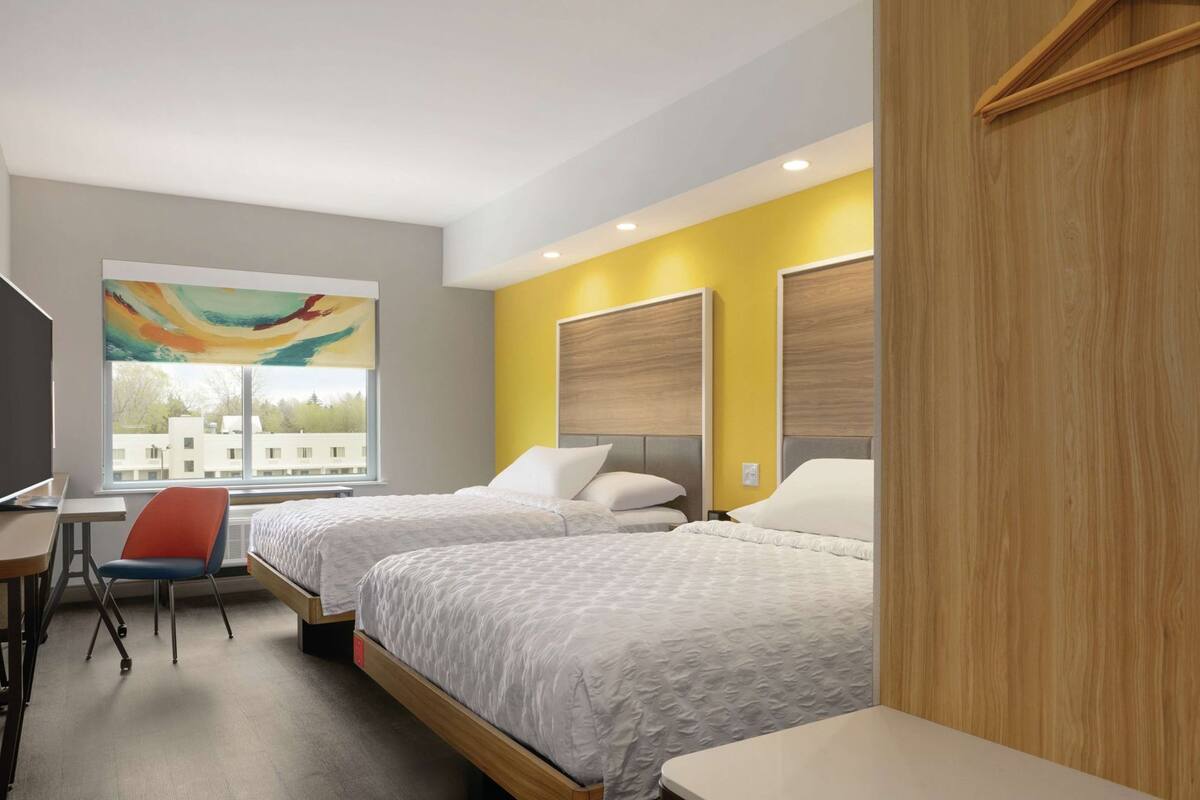 Ein Hotelzimmer mit zwei Betten, einem Schreibtisch, einem Stuhl und einem großen Fenster.