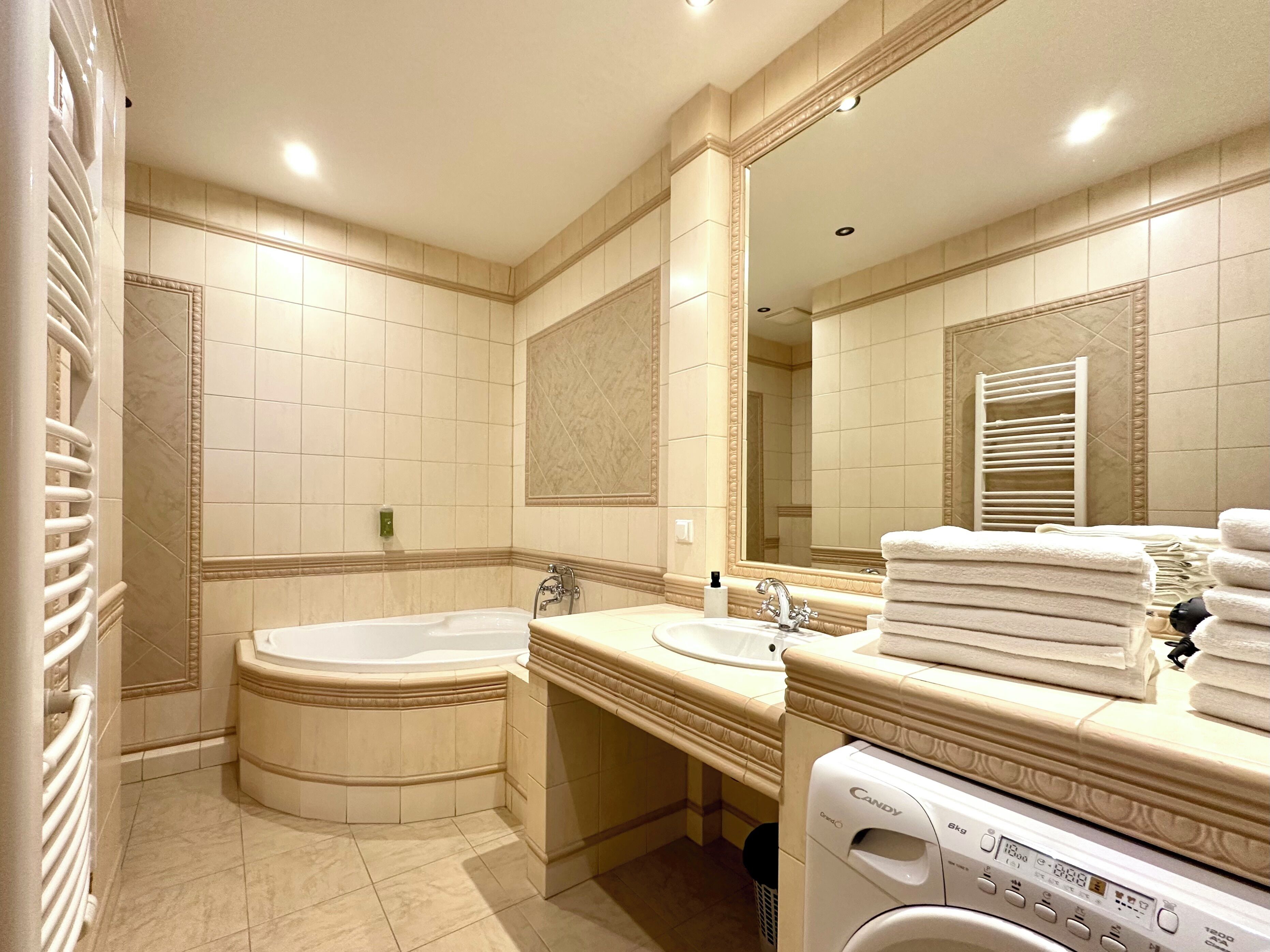 A bathroom with a bathtub, a sink, a mirror, and a stack of towels.