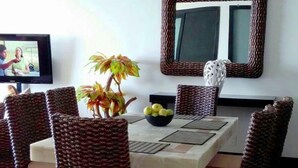 A dining area with a table surrounded by wicker chairs, a ceiling fan, a large mirror, and a TV on the wall. - Bay View Grand Marina 2BR (Ixtapa)