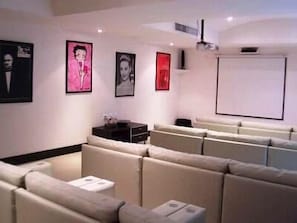 Une salle de cinéma moderne, dotée de sièges confortables, d’un écran de projection et d’œuvres d’art encadrées qui ornent les murs.