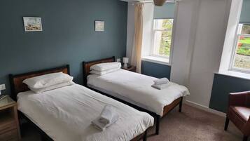 A room with two single beds, a wooden nightstand, a chair, and a window with curtains.