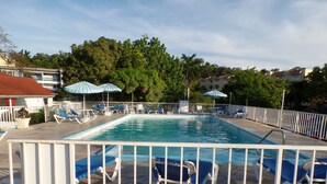 Ein Swimmingpool mit blauen Stühlen und Sonnenschirmen, umgeben von einem weißen Zaun.