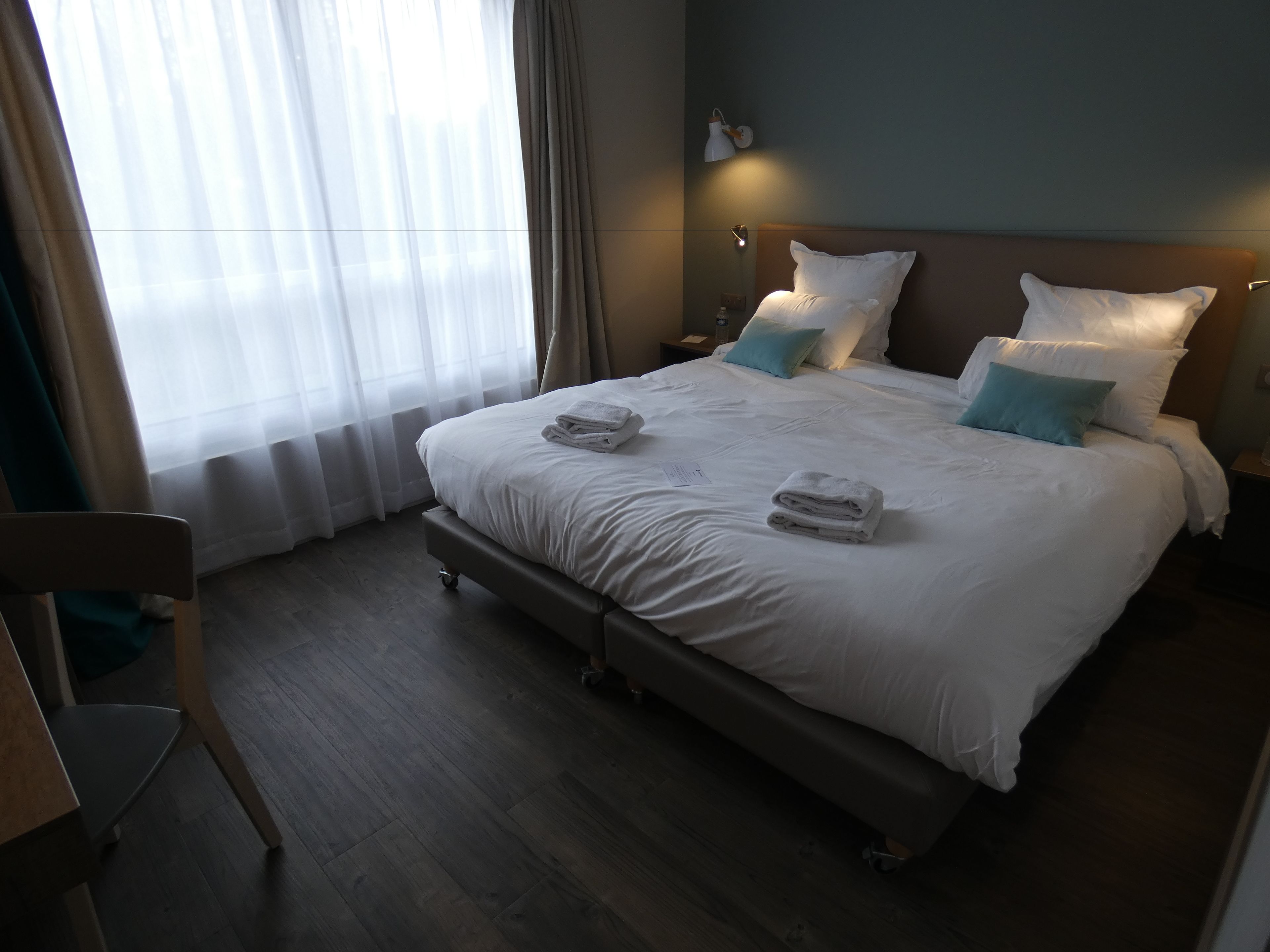 Een hotelkamer met een bed, nachtkastjes, een stoel en een raam met gordijnen.