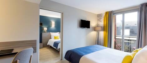 Habitación de hotel con cama, escritorio, silla, televisor y balcón con cortinas.