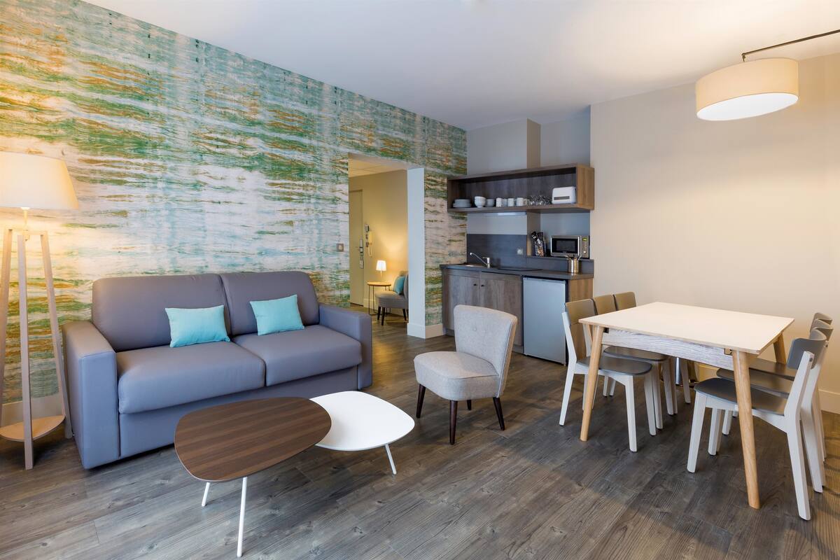 Un salon moderne comprenant un canapé, une table à manger et des chaises. Il y a également un coin cuisine avec des placards et un four à micro-ondes.